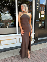 Woman wearing a dark brown satin maxi halter maxi dress with gold trim.