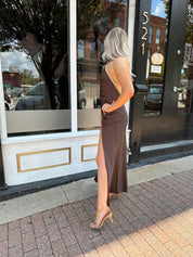 Woman wearing a dark brown satin maxi halter maxi dress with gold trim.