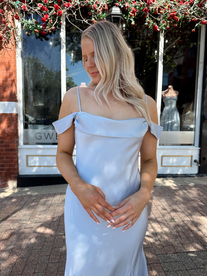 Woman wearing light blue satin midi dress with adjustable straps, and off the shoulder sleeves.