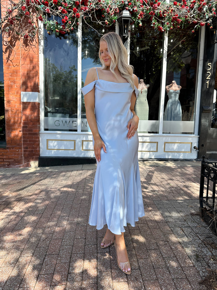 Woman wearing light blue satin midi dress with adjustable straps, and off the shoulder sleeves.