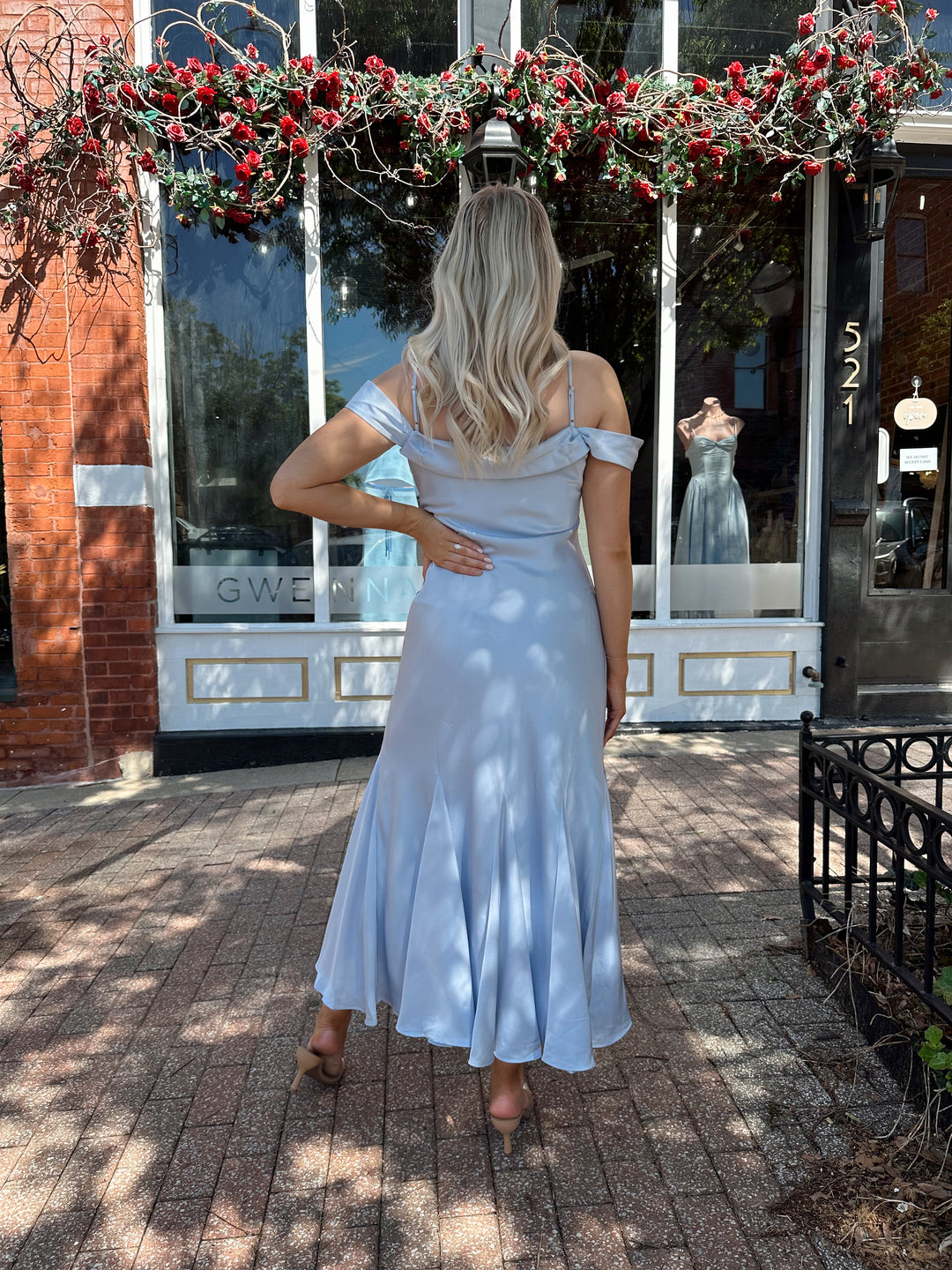 Woman wearing light blue satin midi dress with adjustable straps, and off the shoulder sleeves.