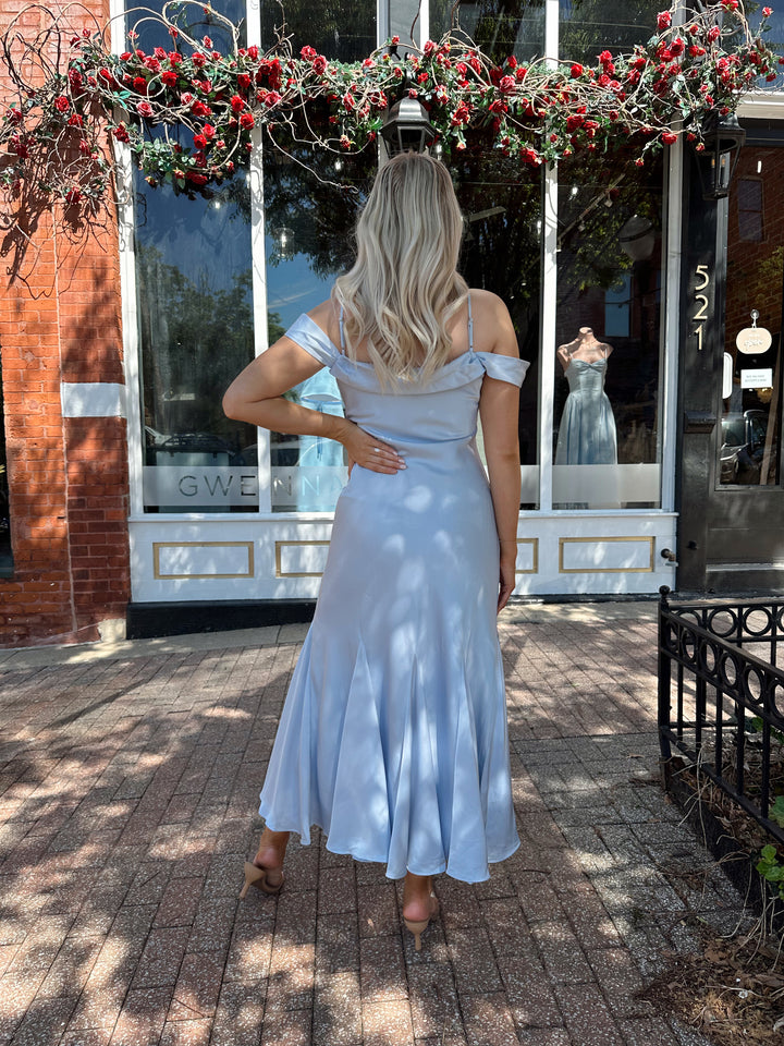 Woman wearing light blue satin midi dress with adjustable straps, and off the shoulder sleeves.