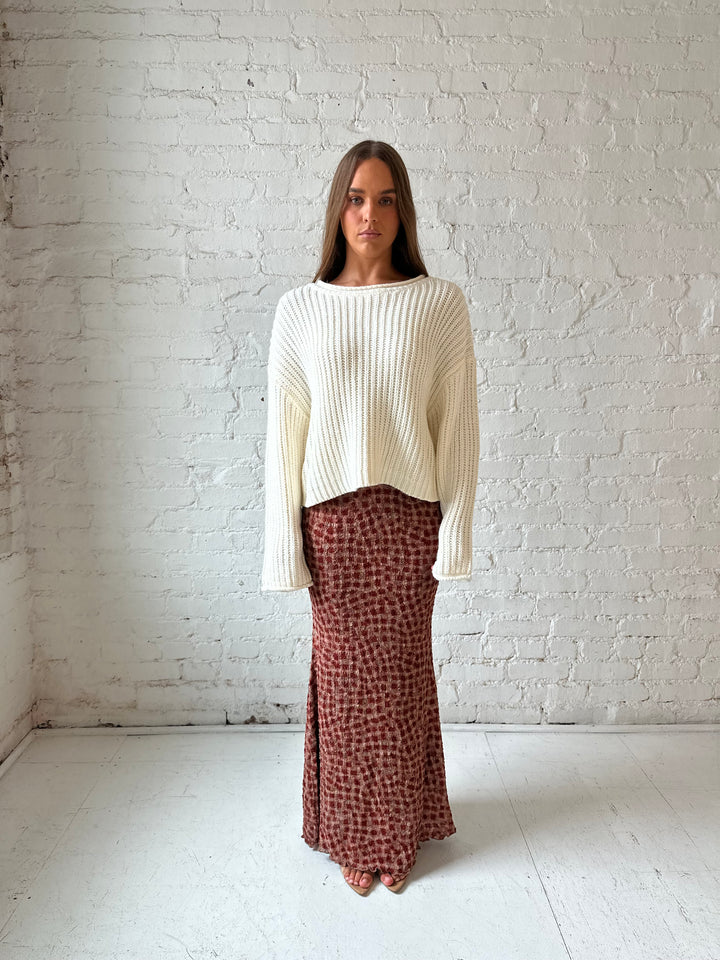 Woman wearing cream knit sweater with burgundy textured dotted maxi skirt.