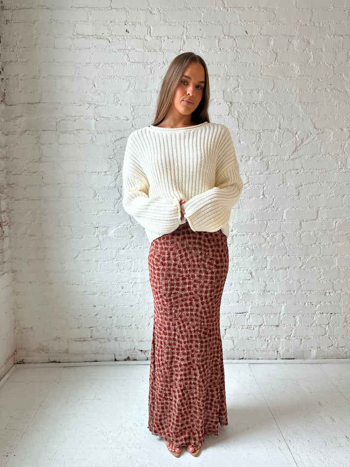 Woman wearing cream knit sweater with burgundy textured dotted maxi skirt.