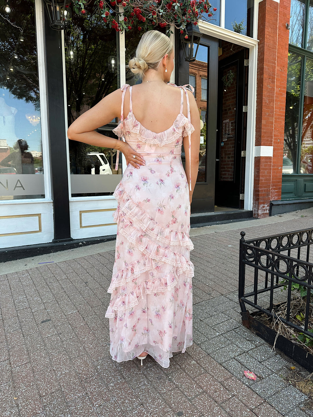 Woman wearing light pink floral ruffle tiered maxi dress with lace trim, and self tie straps.