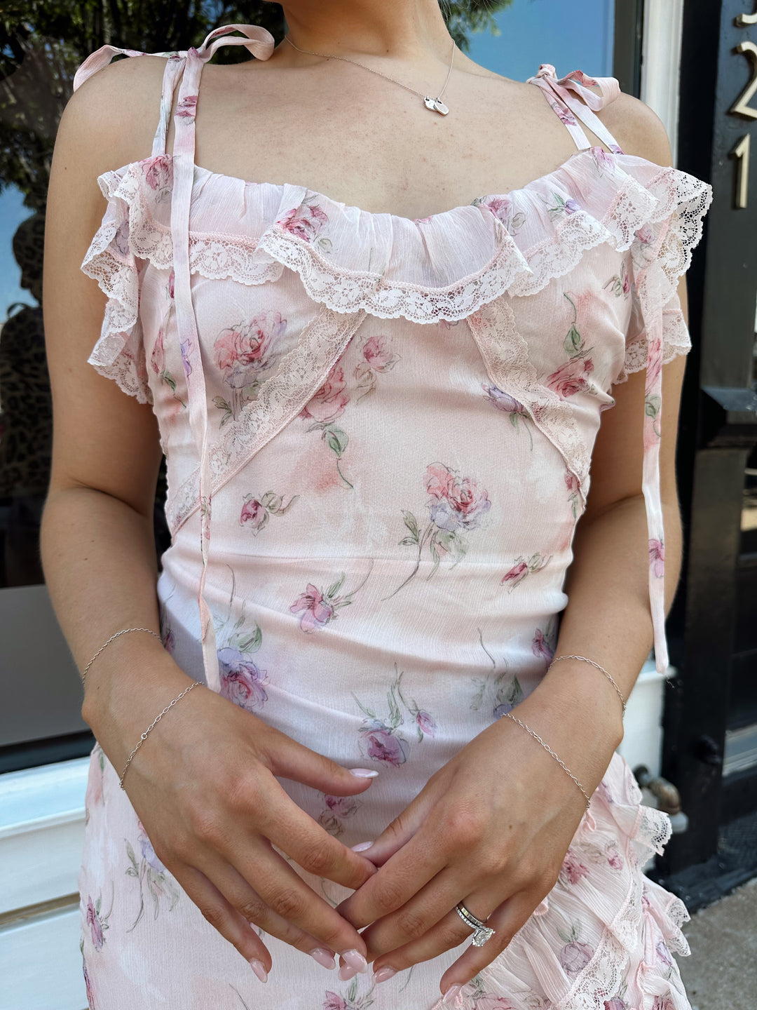 Woman wearing light pink floral ruffle tiered maxi dress with lace trim, and self tie straps.