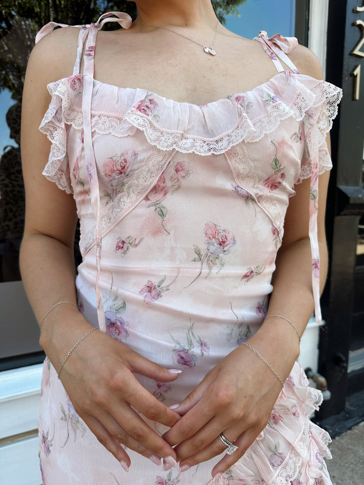 Woman wearing light pink floral ruffle tiered maxi dress with lace trim, and self tie straps.