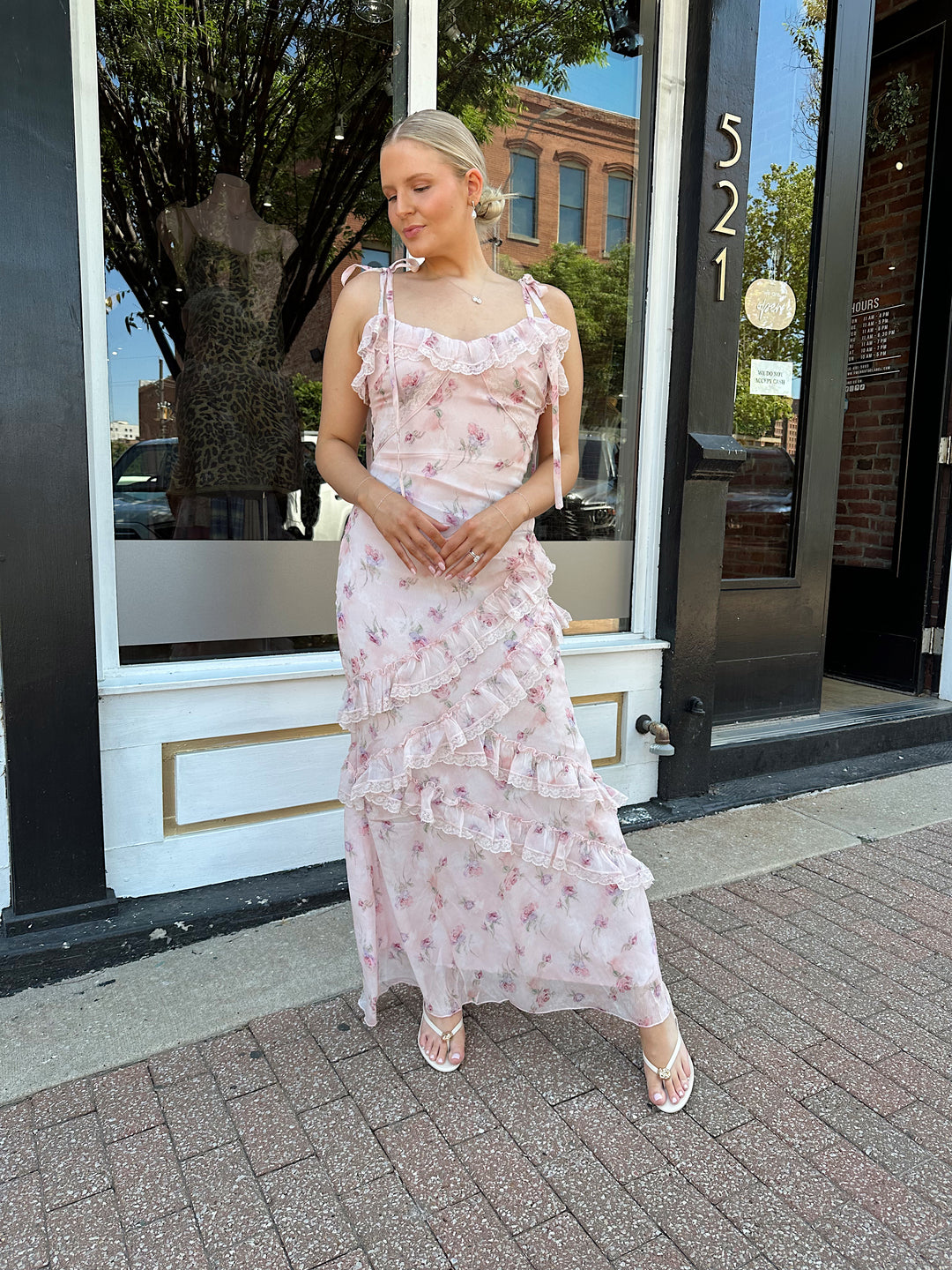 Woman wearing light pink floral ruffle tiered maxi dress with lace trim, and self tie straps.