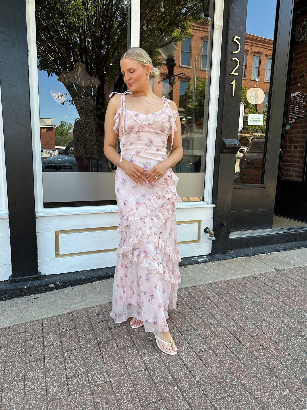 Woman wearing light pink floral ruffle tiered maxi dress with lace trim, and self tie straps.