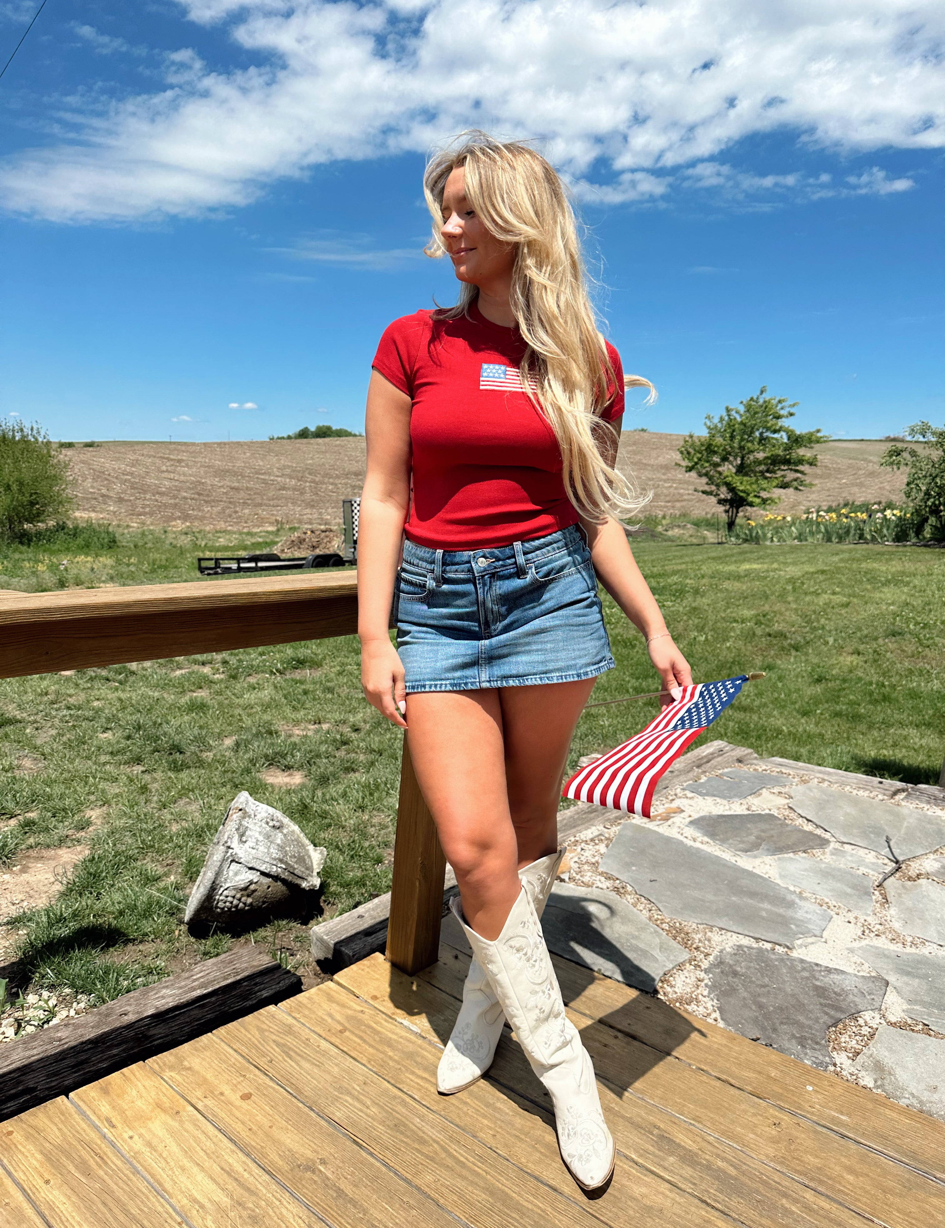 Woman in a red baby tee with an embroidered American flag, styled with a denim mini skirt