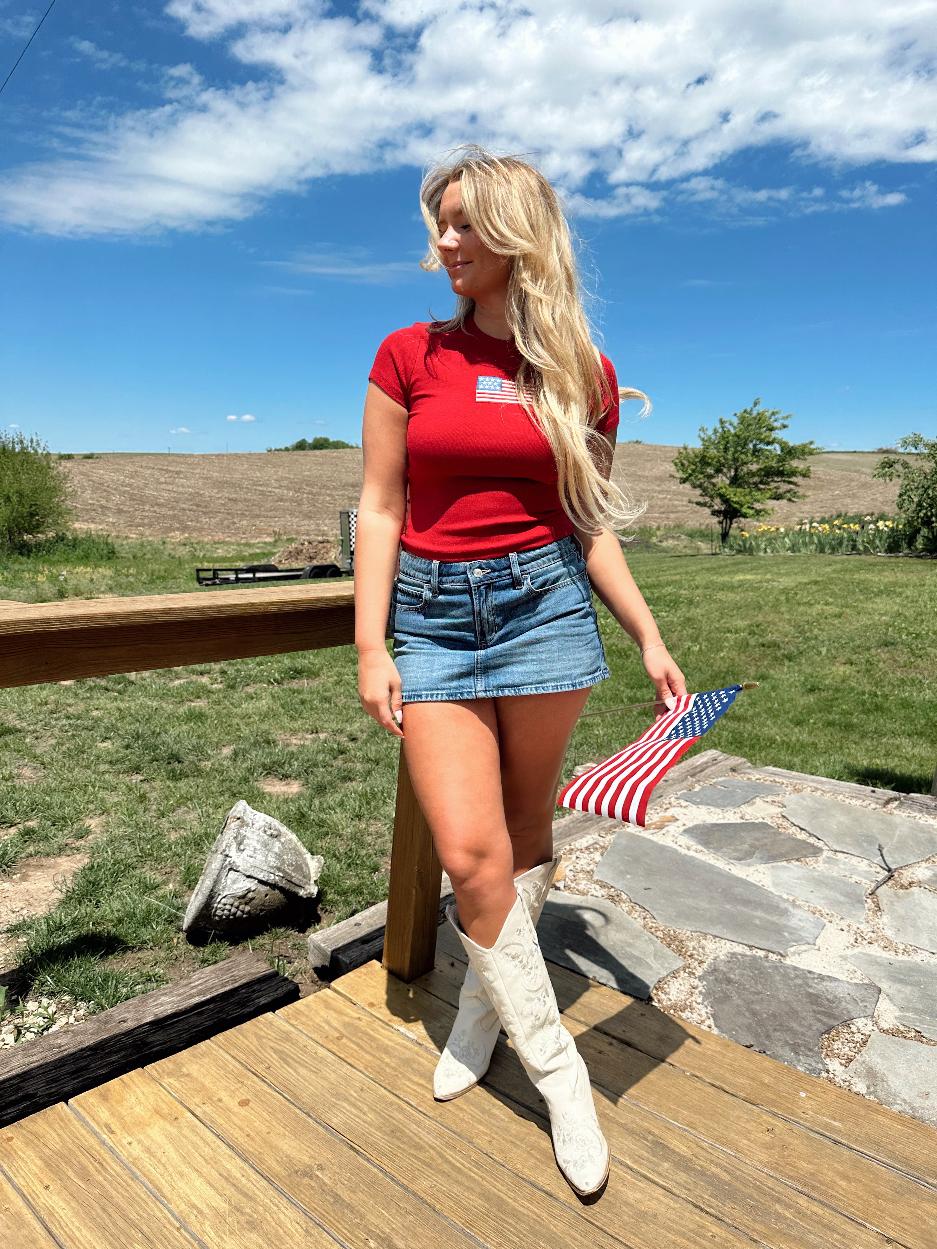 Woman in a red baby tee with an embroidered American flag, styled with a denim mini skirt