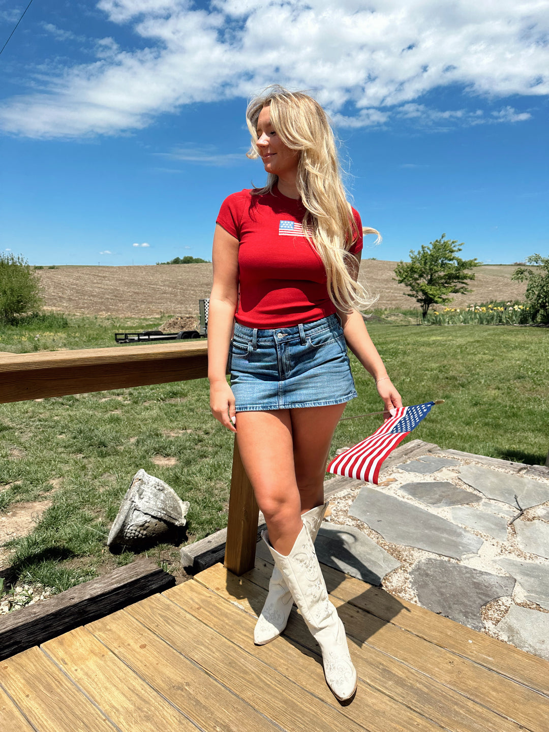 Woman in a red baby tee with an embroidered American flag, styled with a denim mini skirt