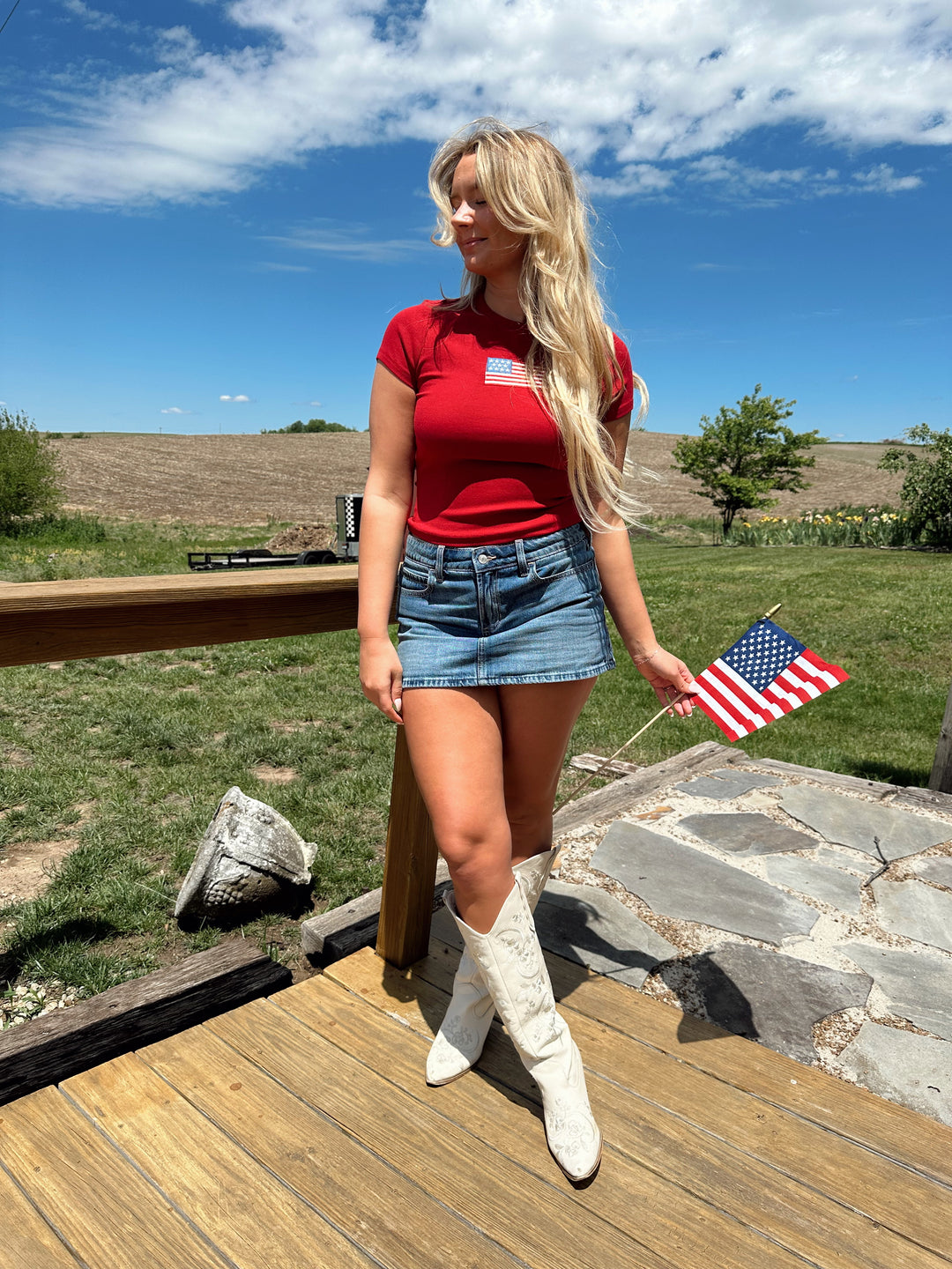 Woman in a red baby tee with an embroidered American flag, styled with a denim mini skirt