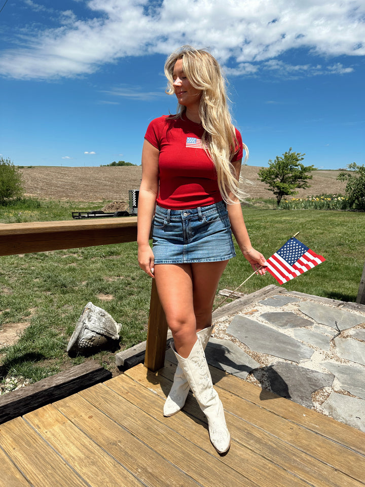 Woman in a red baby tee with an embroidered American flag, styled with a denim mini skirt