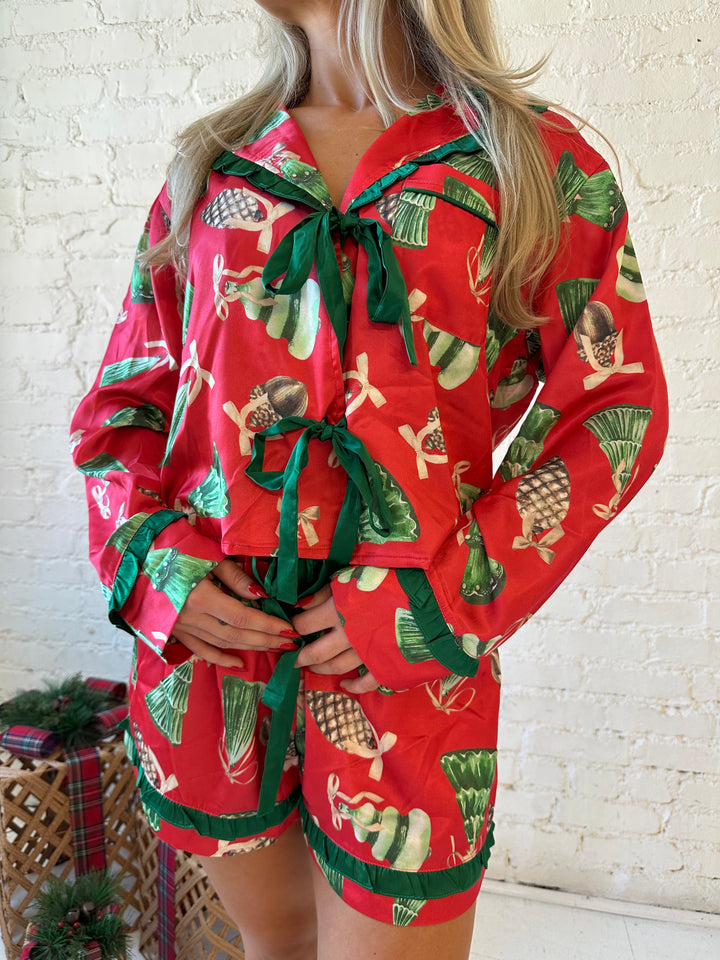Woman wearing red satin pajama set with ornaments all over.