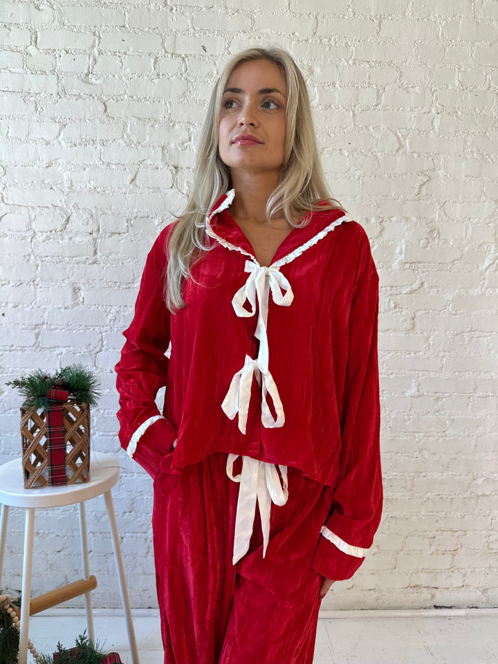 Woman wearing red velvet pajama set with long sleeve, and front tie closure. 