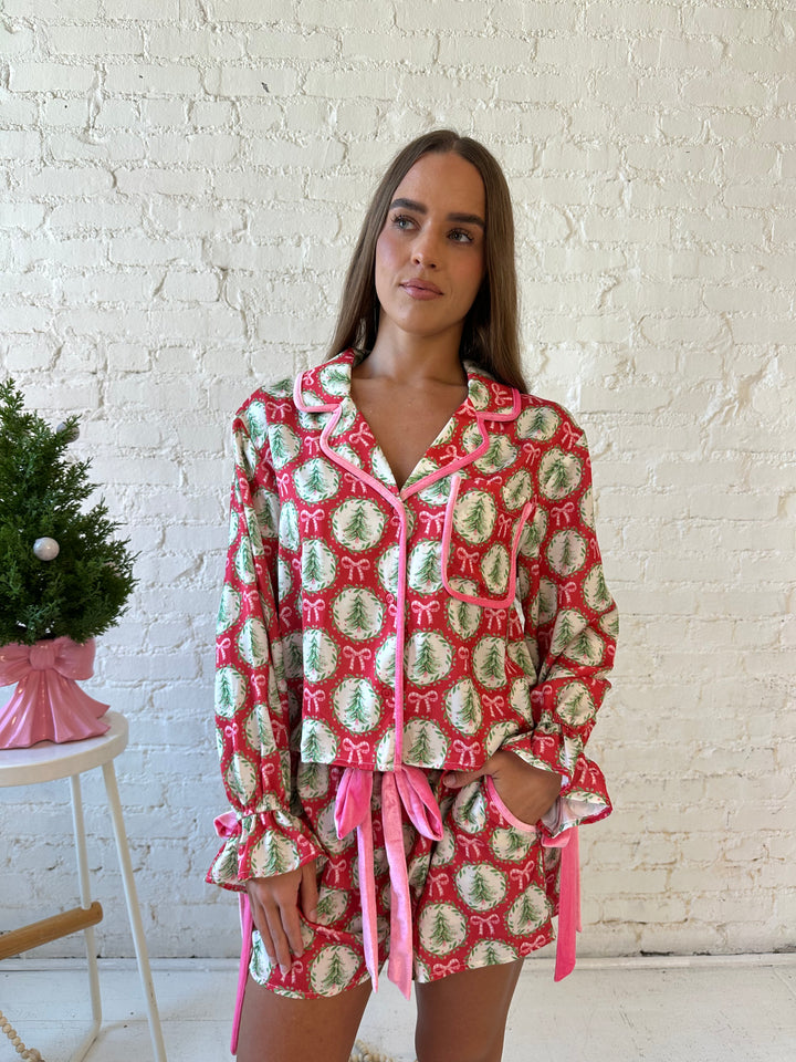 Woman wearing red satin pajamas with pink and green Christmas trees and wreaths all over. 