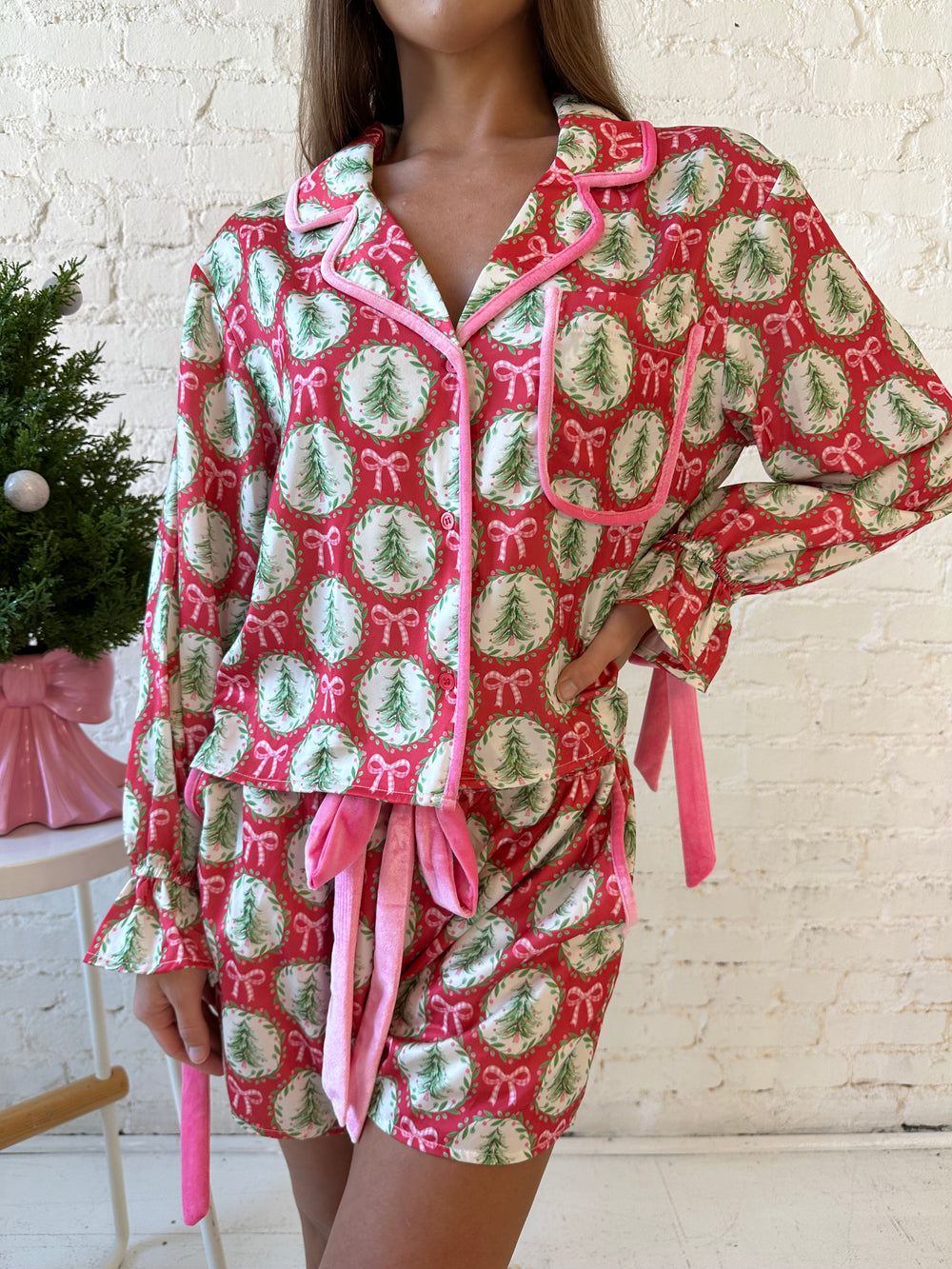 Woman wearing red satin pajamas with pink and green Christmas trees and wreaths all over. 