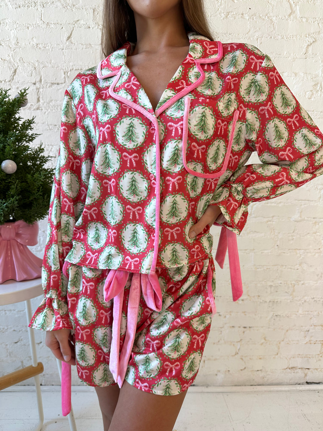 Woman wearing red satin pajamas with pink and green Christmas trees and wreaths all over. 