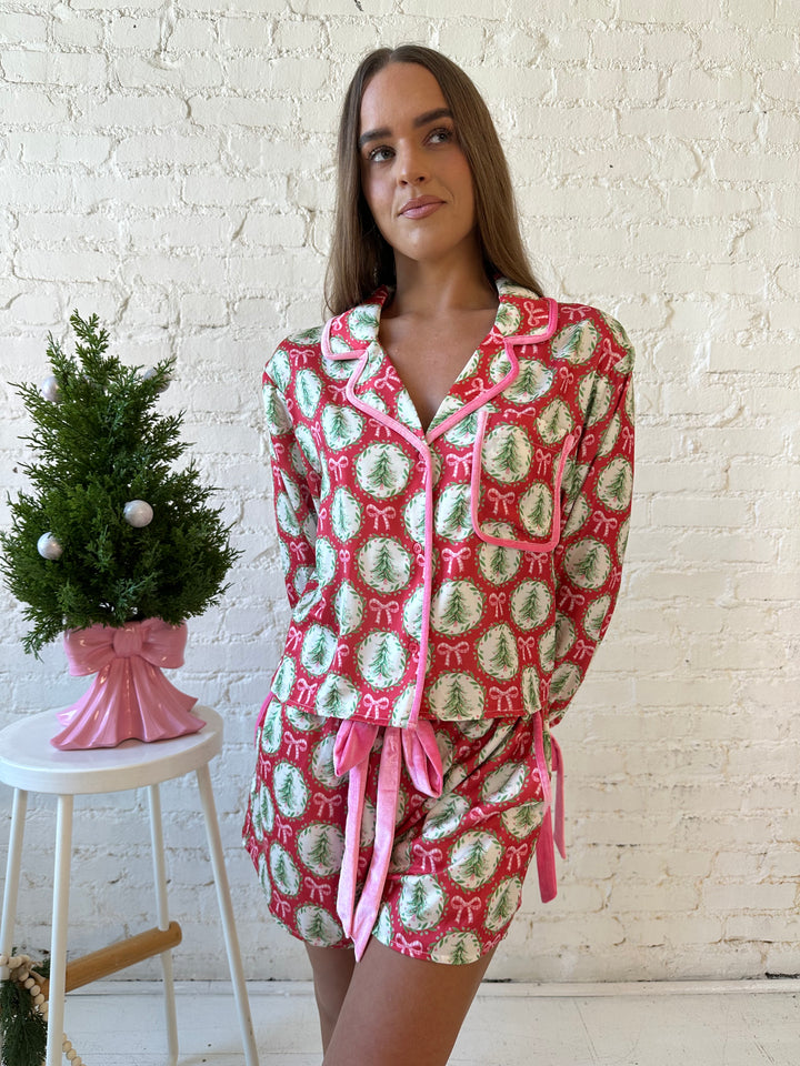 Woman wearing red satin pajamas with pink and green Christmas trees and wreaths all over. 