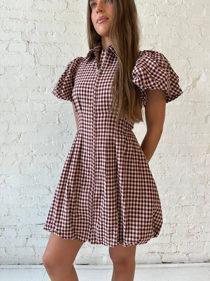 Woman wearing burgundy plaid mini dress with collar zipper neckline, short sleeves, and bubble hem.