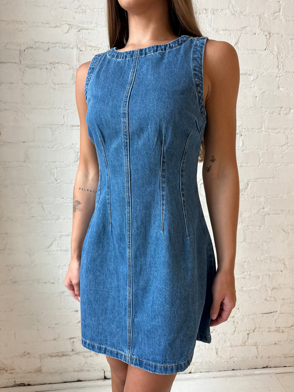 Woman wearing dark wash denim mini dress with front stitching, and cream knee boots.