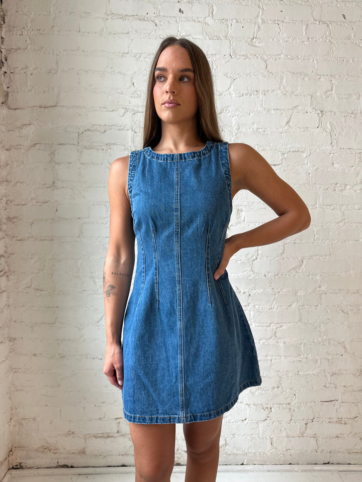 Woman wearing dark wash denim mini dress with front stitching, and cream knee boots.