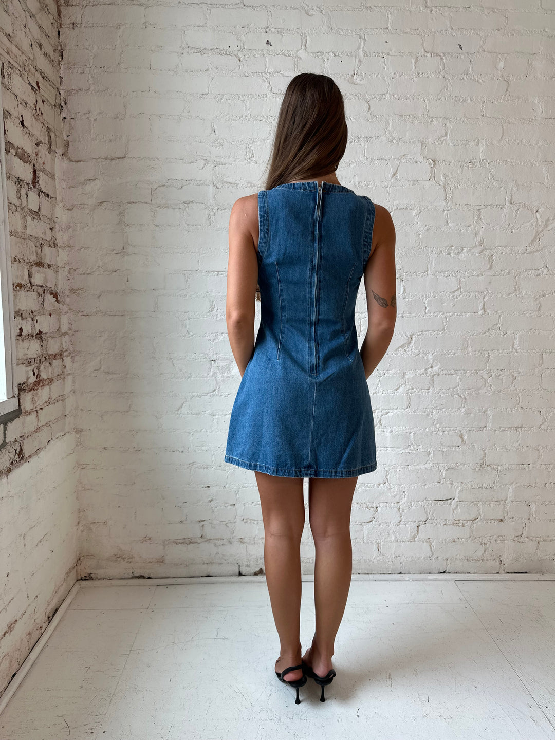 Woman wearing dark wash denim mini dress with front stitching, and cream knee boots.