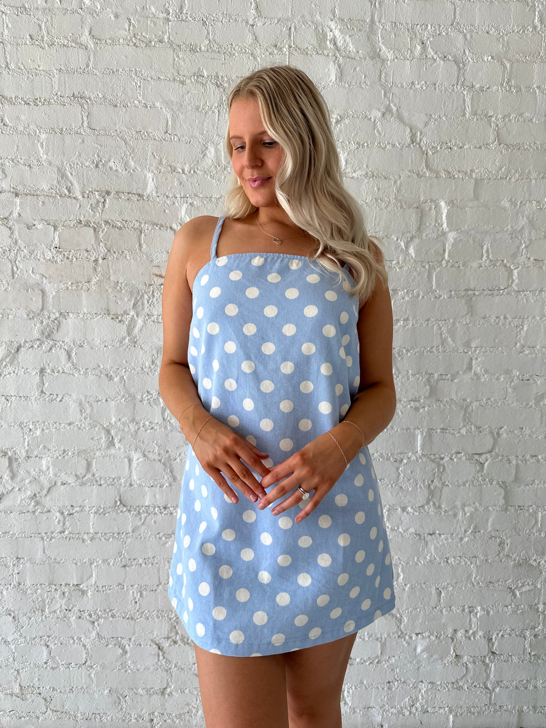Woman wearing sky blue polka dot denim mini dress with straight neckline and adjustable straps.
