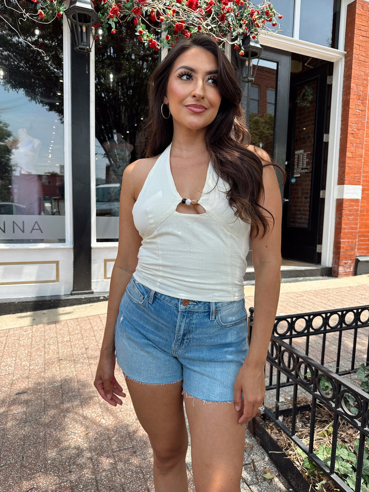 Woman wearing ivory halter top with headed detailing, and denim shorts.