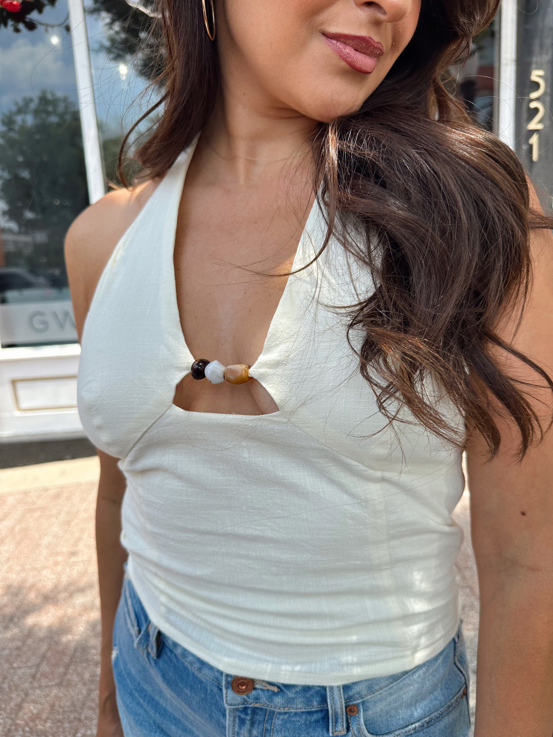 Woman wearing ivory halter top with headed detailing, and denim shorts.