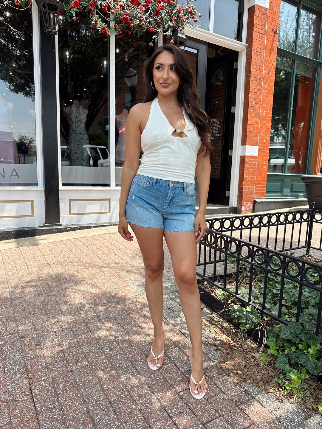 Woman wearing ivory halter top with headed detailing, and denim shorts.