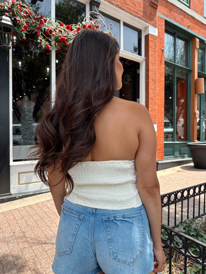 Woman wearing ivory halter top with headed detailing, and denim shorts.