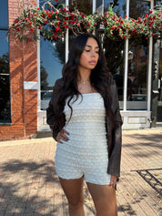 Woman wearing ivory textured strapless romper with brown leather blazer.
