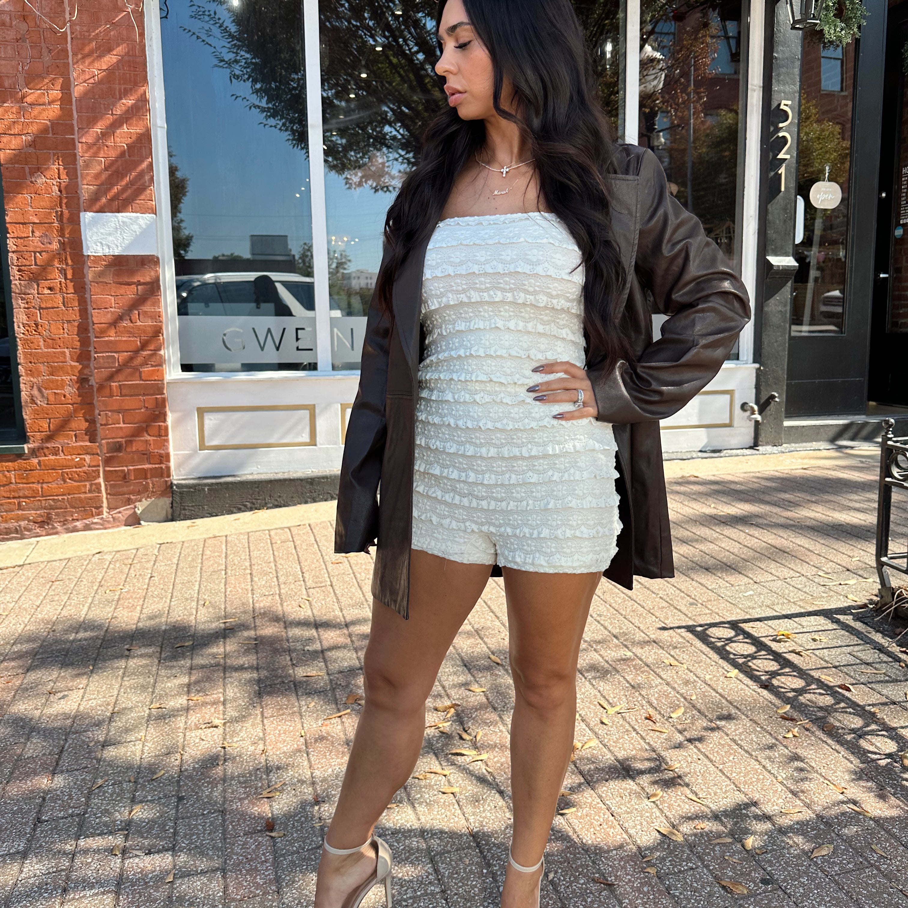 Woman wearing ivory textured strapless romper with brown leather blazer.
