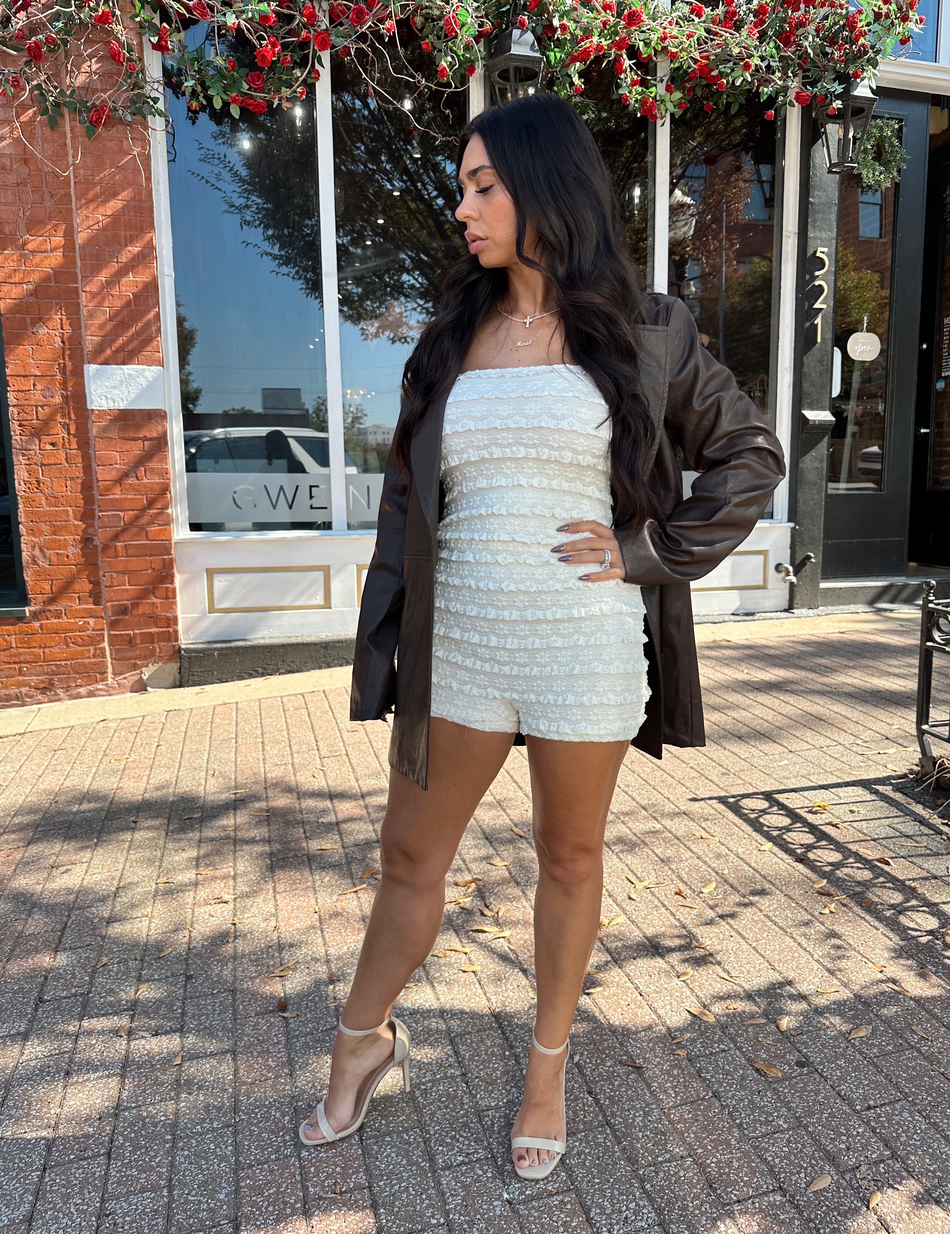 Woman wearing ivory textured strapless romper with brown leather blazer.