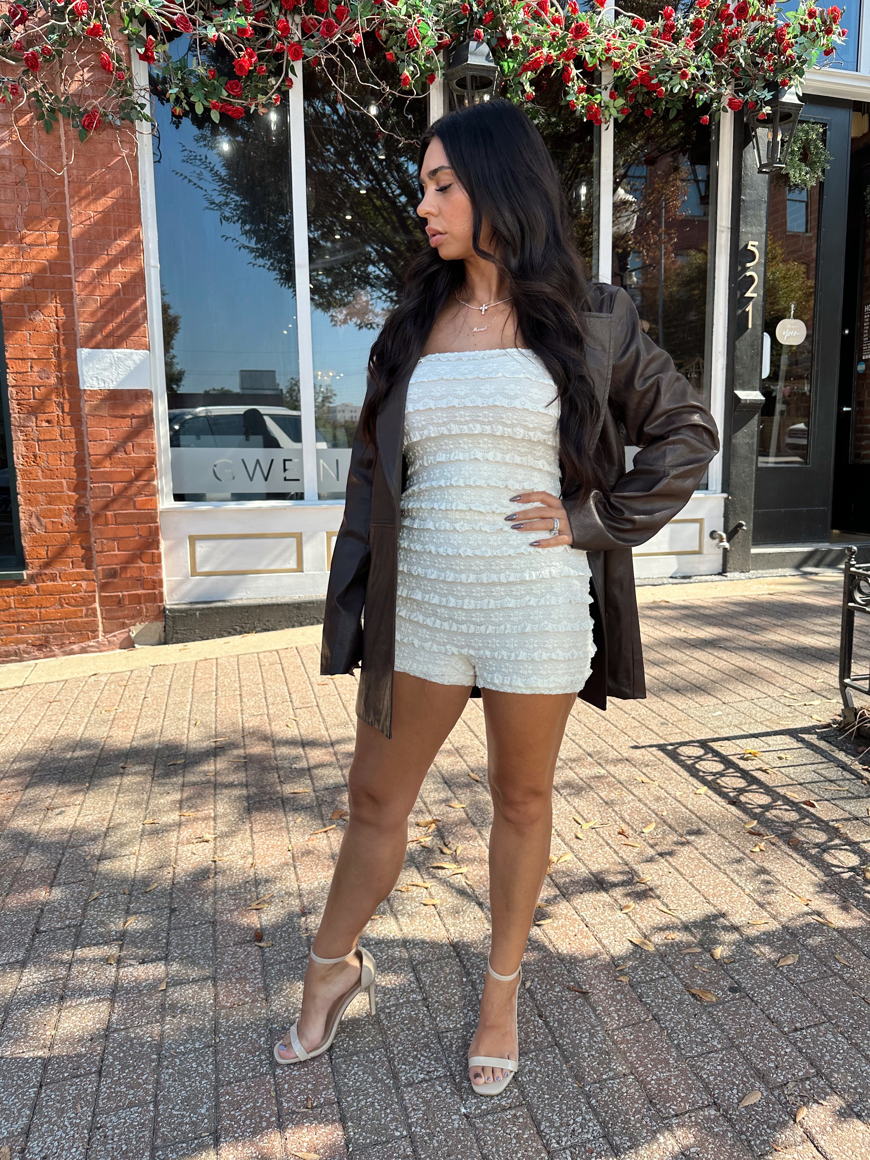 Woman wearing ivory textured strapless romper with brown leather blazer.