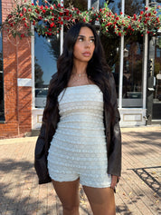 Woman wearing ivory textured strapless romper with brown leather blazer.