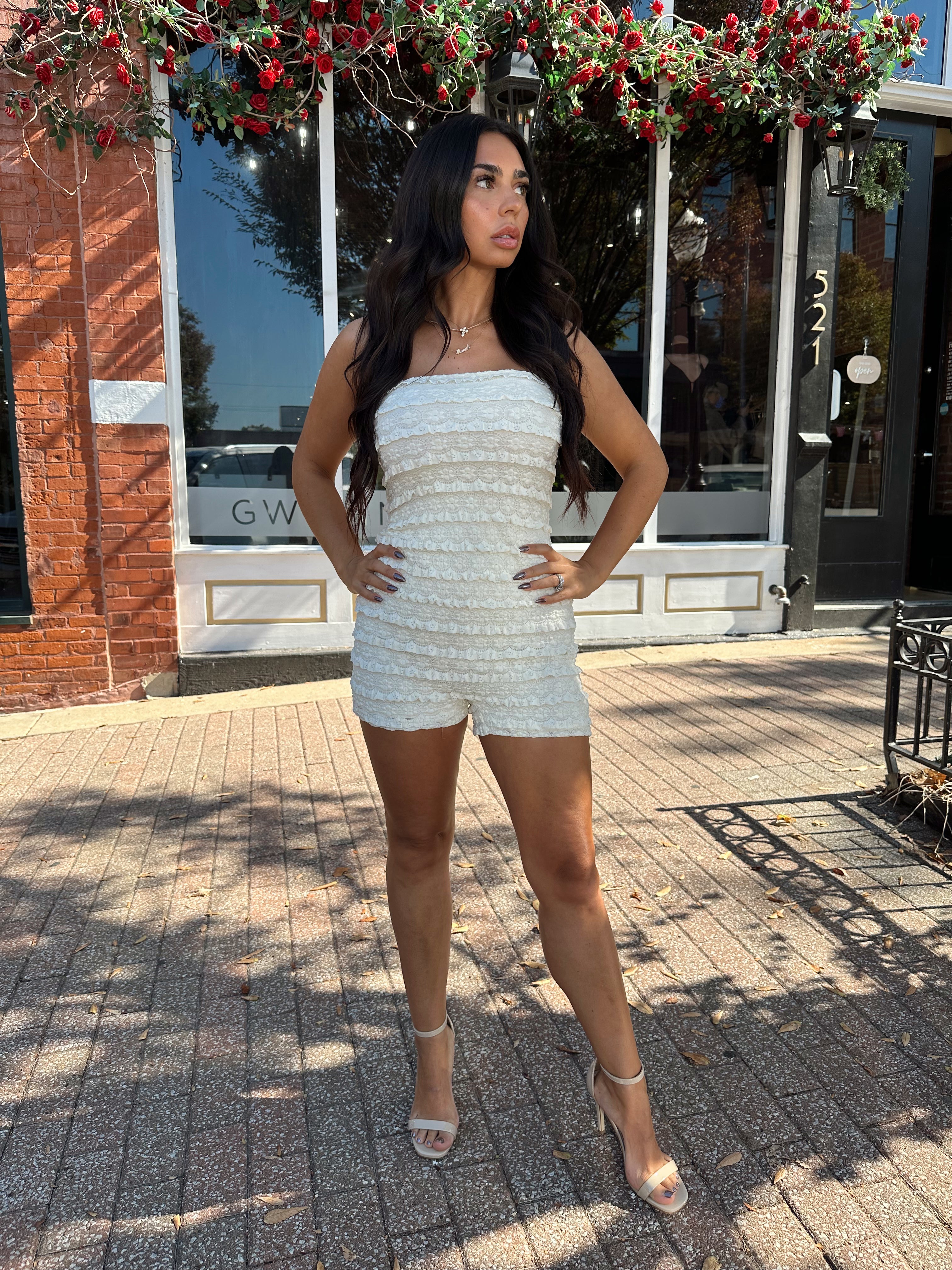 Woman wearing ivory textured strapless romper with brown leather blazer.