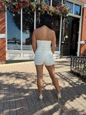 Woman wearing ivory textured strapless romper with brown leather blazer.
