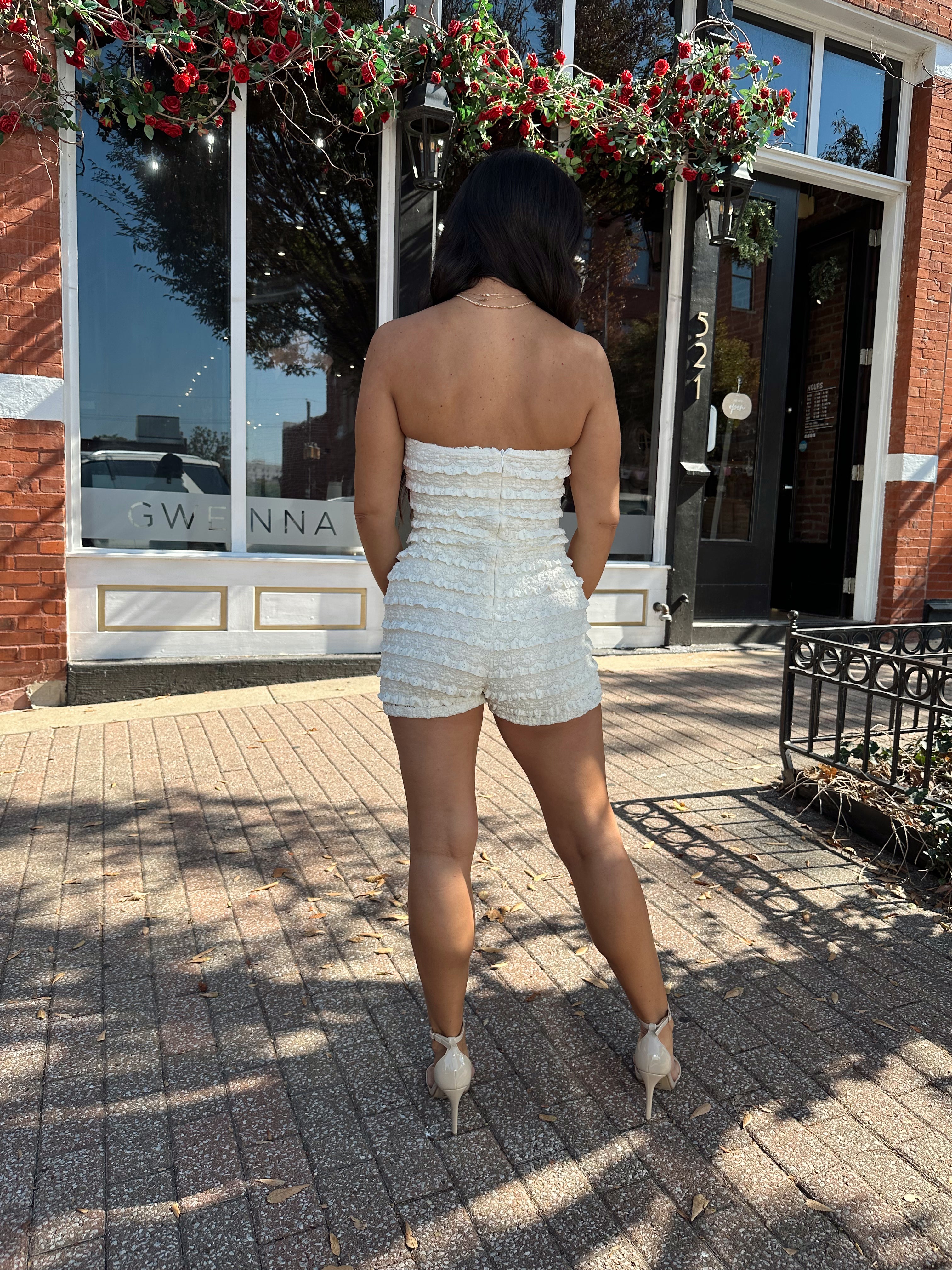 Woman wearing ivory textured strapless romper with brown leather blazer.