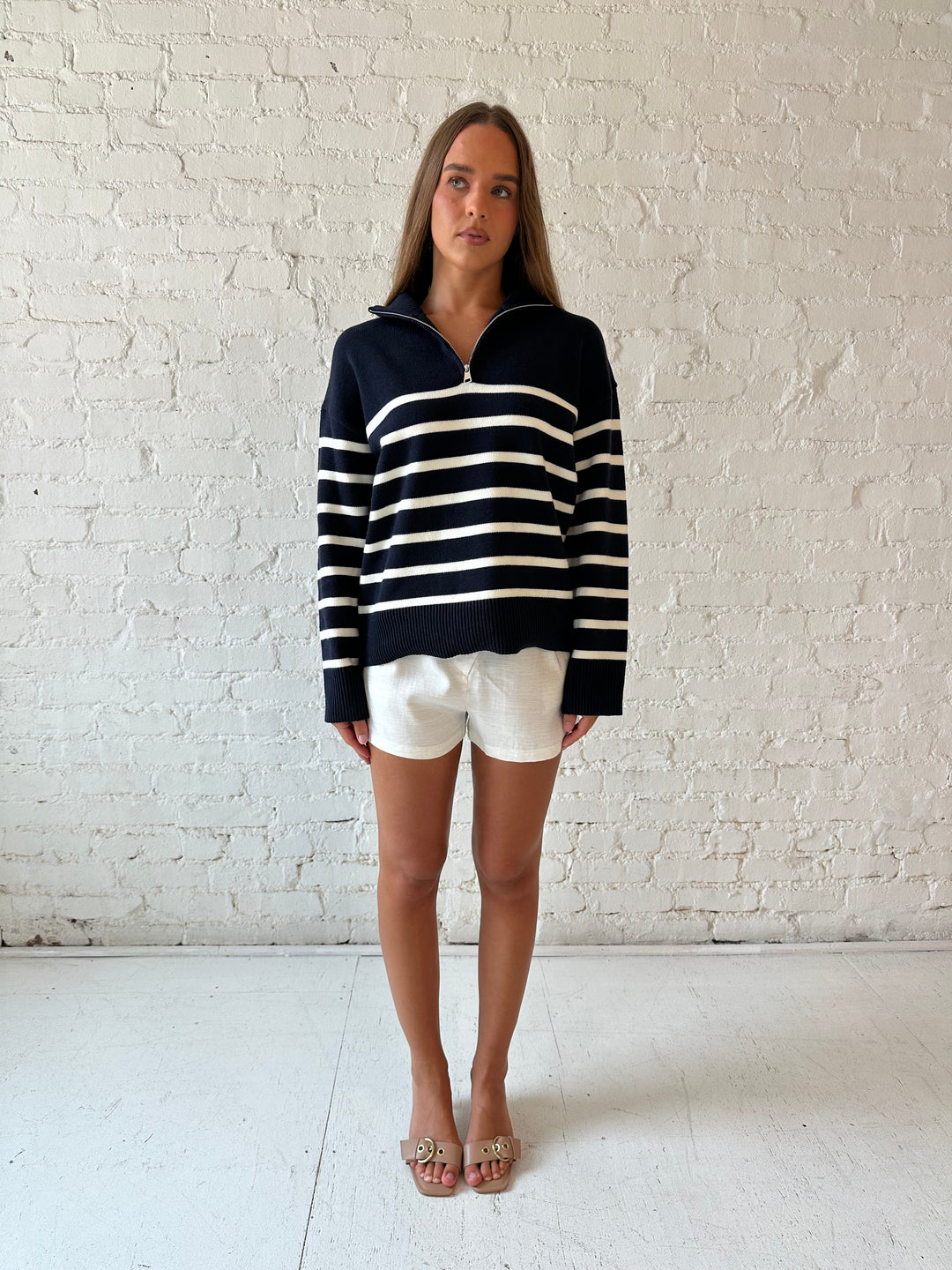 Woman wearing navy and cream striped quarter zip sweater with cream shorts. 