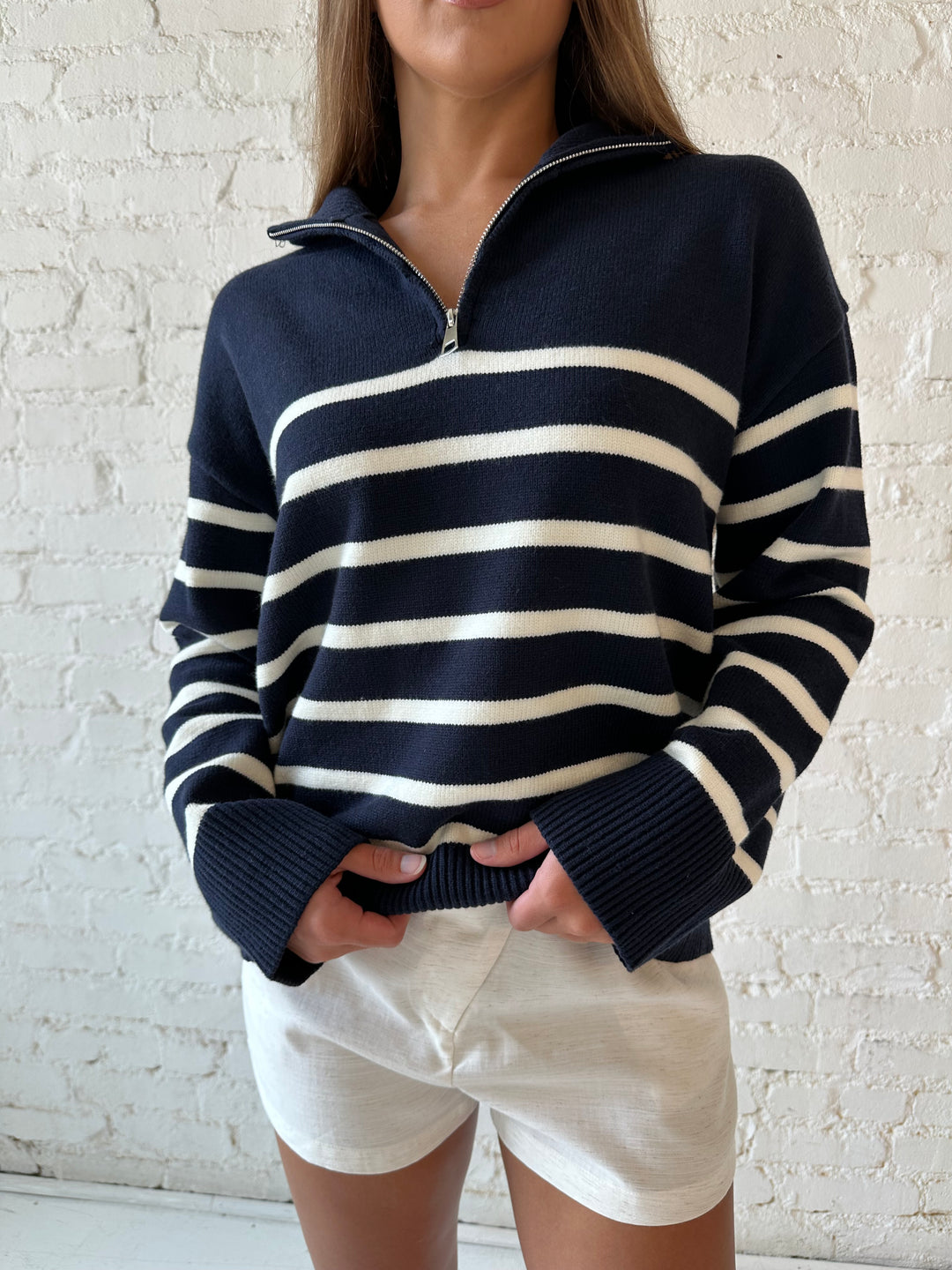 Woman wearing navy and cream striped quarter zip sweater with cream shorts. 