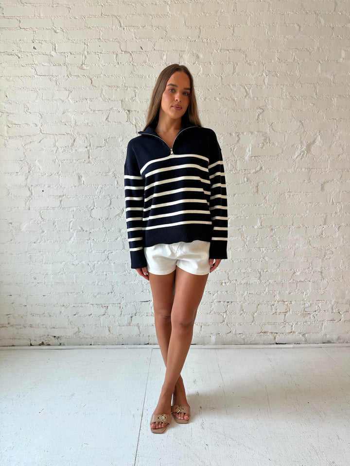 Woman wearing navy and cream striped quarter zip sweater with cream shorts. 