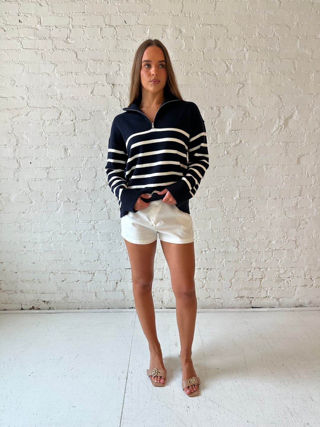 Woman wearing navy and cream striped quarter zip sweater with cream shorts. 