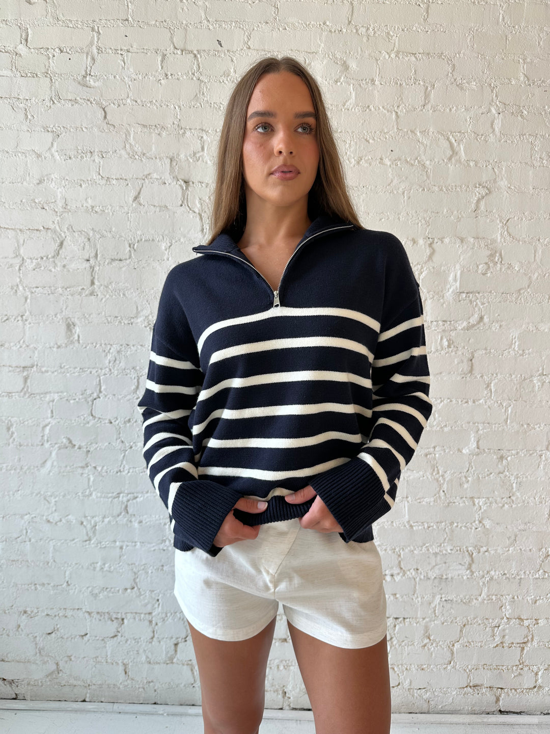 Woman wearing navy and cream striped quarter zip sweater with cream shorts. 