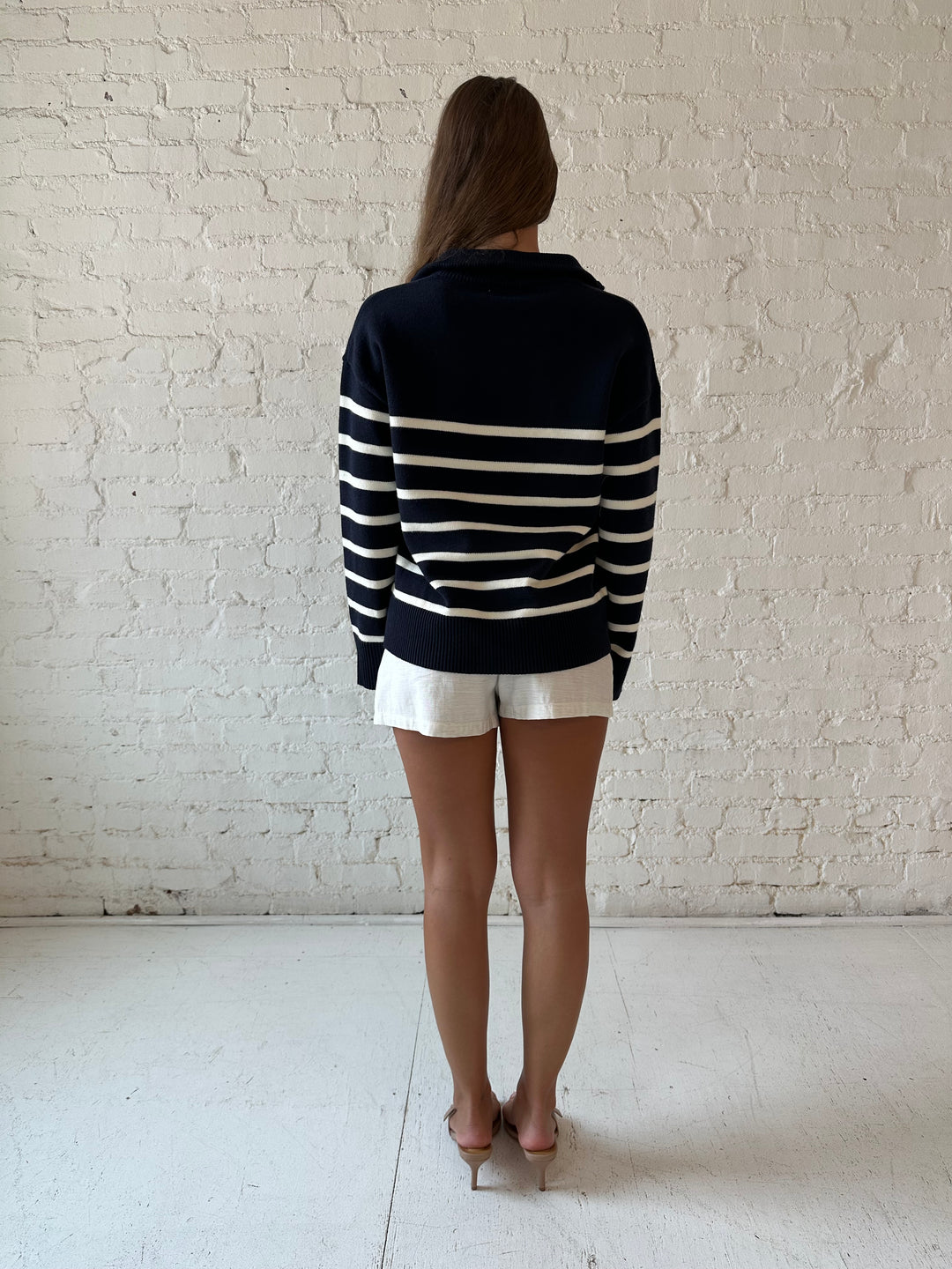 Woman wearing navy and cream striped quarter zip sweater with cream shorts. 