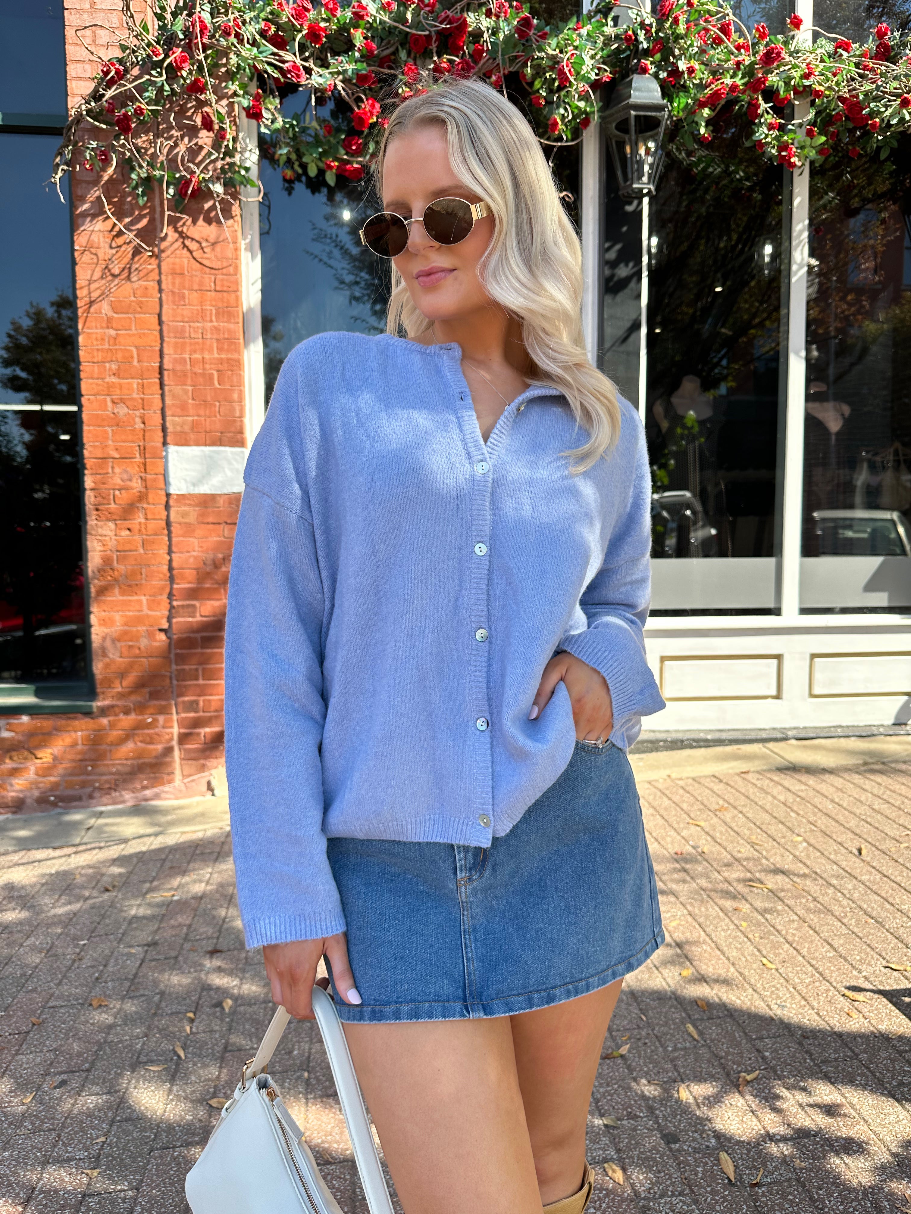 Woman wearing baby blue knit button down cardigan with denim skirt. 