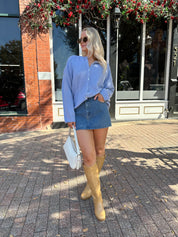 Woman wearing baby blue knit button down cardigan with denim skirt. 