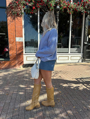 Woman wearing baby blue knit button down cardigan with denim skirt. 